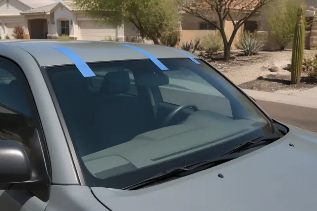 Newly installed windshield held by retention tape on a vehicle in Phoenix, AZ, with xeriscaping in the background.