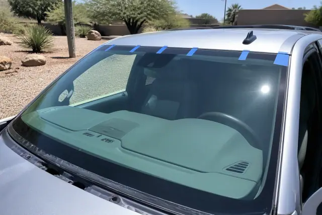 New windshield installed on a vehicle with retention tape in a sunny Phoenix, AZ desert landscape.