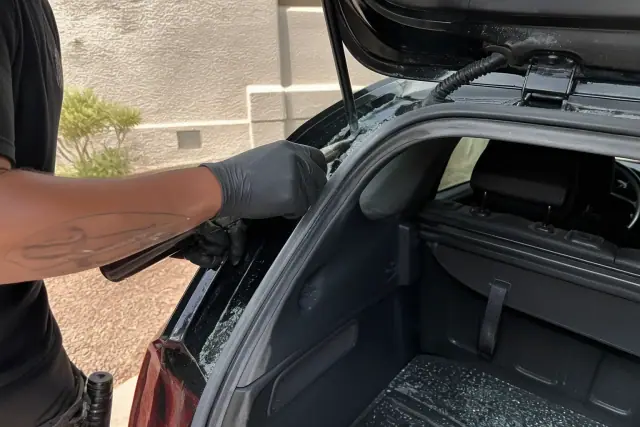 Technician removing broken rear hatchback glass from weather stripping at a job site in Phoenix, AZ.
