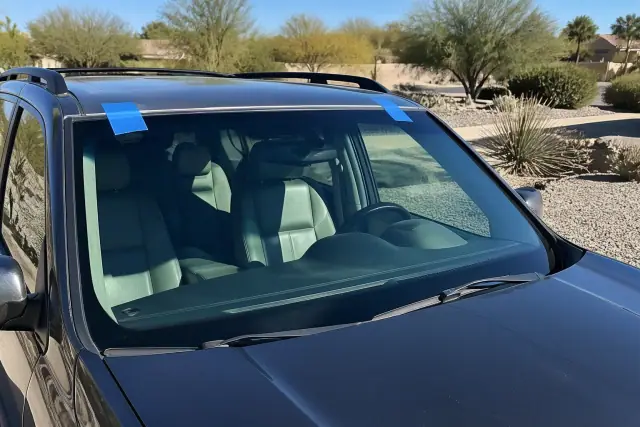 Newly installed car windshield held by blue retention tape in Phoenix, AZ, with desert landscaping in the background.