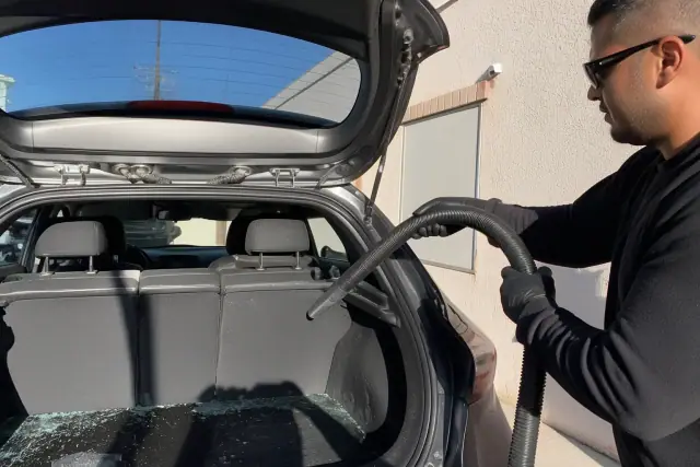 Technician vacuuming glass shards from the rear window weather stripping of a car in Phoenix, AZ.
