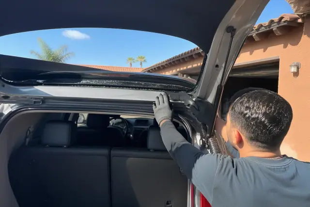 Technician removing broken rear windshield glass from a hatchback at a job site in Glendale, AZ.