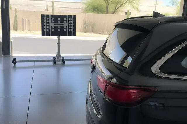 Technician performing ADAS calibration on a vehicle in a Phoenix, AZ service bay with a digital target stand.
