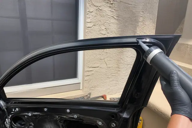 Technician applying adhesive to a car window frame during a side glass replacement in Phoenix, AZ.