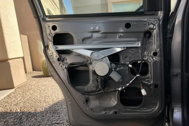 Car door interior with the trim removed to show the window regulator and motor during repair in Phoenix, AZ.