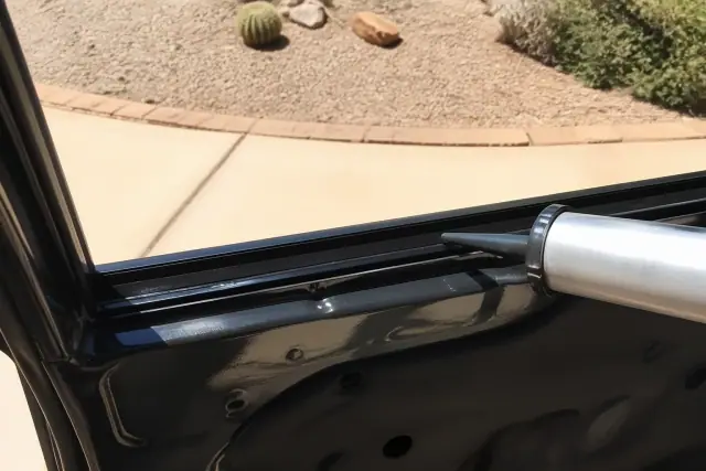Contractor applying adhesive to a door window frame for side glass replacement in Goodyear, AZ.