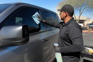 Technician using a microfiber cloth to clean a new side door window on a car in Phoenix, AZ.