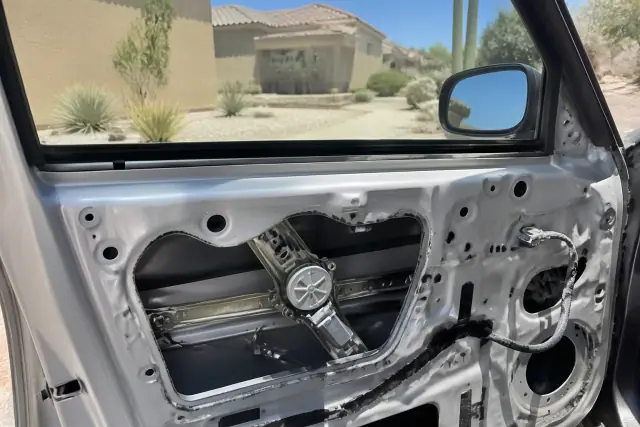 Vehicle door with interior panel removed exposing the window regulator and electric motor during repair in Peoria, AZ.