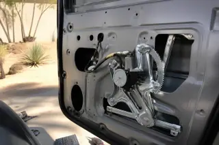 Exposed mechanical window regulator and electric motor inside a car door frame in Phoenix, AZ.
