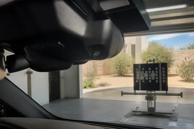Vehicle windshield camera and sensor housing with an exterior view of a Phoenix, AZ service bay in the background.