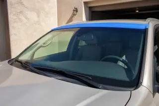 Newly installed car windshield with retention tape against a sunlit stucco garage in Phoenix, AZ.