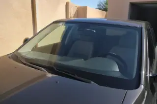A clean, newly installed windshield on a car parked outside a stucco home in Phoenix, AZ.