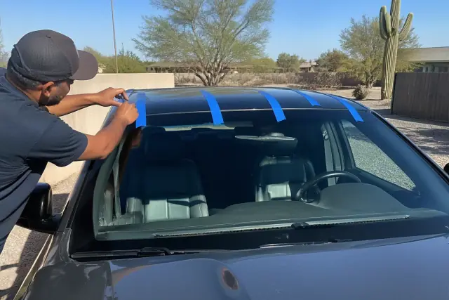 Technician applying retention tape to a newly installed windshield on a vehicle in Peoria, AZ.