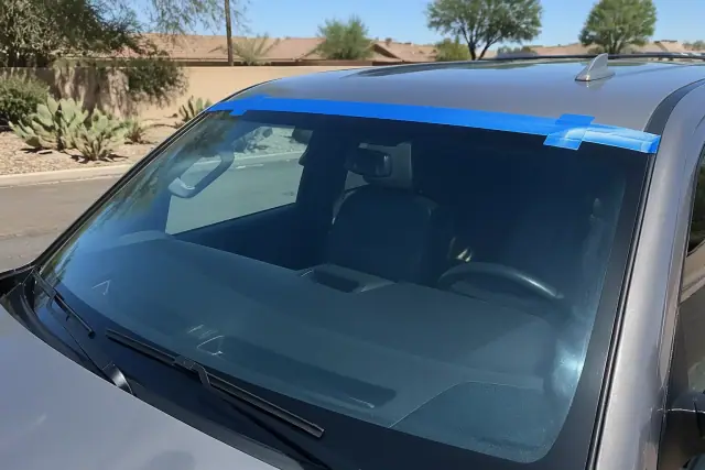 New windshield with retention tape on a car parked in Tempe, AZ with prickly pear cactus in the background.