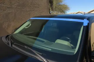 New windshield with retention tape on a car parked against a stucco wall in Phoenix, AZ.