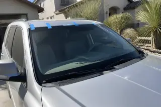 Newly installed windshield with retention tape on a car parked in front of a xeriscaped yard in Phoenix, AZ.