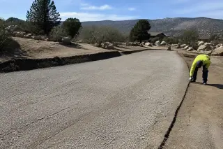 Worker inspecting a milled asphalt base layer near granite boulders and desert brush in Prescott, AZ.