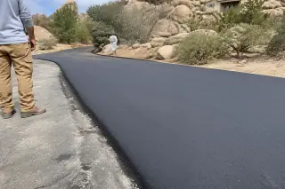 Worker checking the edge of a new asphalt driveway next to granite boulders in Prescott, AZ.