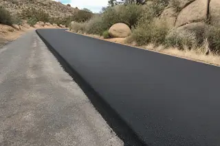 Newly paved asphalt driveway meeting older pavement next to granite boulders in Prescott, AZ.