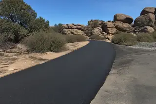 Freshly paved asphalt driveway with a clean transition to old pavement near granite boulders in Prescott, AZ.