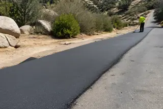 Technician inspecting a new asphalt strip near granite rocks and desert scrub in Prescott, AZ.
