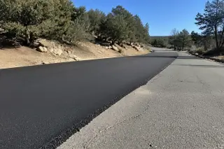 Fresh black asphalt overlay meeting existing pavement near juniper trees and scrub oak in Prescott, AZ.