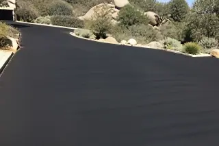 Deep black sealcoated driveway surface next to high-desert granite boulders in Prescott, AZ.