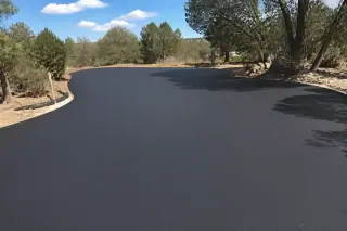 Deep black sealcoated asphalt driveway surrounded by scrub oak, pine trees, and granite soil in Prescott, AZ.
