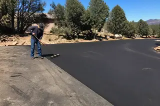 Contractor sweeping a new asphalt driveway transition near granite landscape in Prescott, AZ.