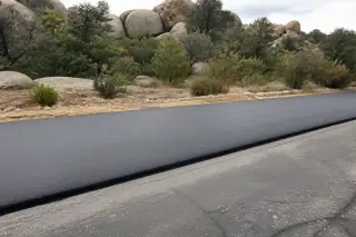 Smooth new asphalt strip meeting existing pavement near granite boulders and desert brush in Prescott, AZ.