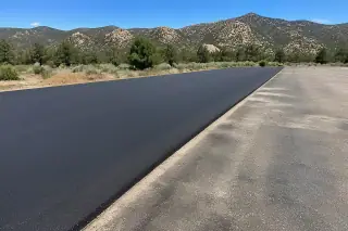 Fresh asphalt patch bordering old pavement with desert scrub and granite mountains in Prescott, AZ.