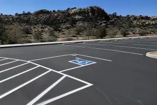Thermoplastic parking lot lines on fresh asphalt with granite boulders and high-desert scrub in Prescott, AZ.