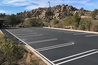 Freshly painted white parking lot lines on a new asphalt surface near granite boulders in Prescott, AZ.