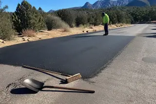 Technician inspecting a finished pothole repair with a shovel and broom on the asphalt in Prescott, AZ.