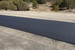 Fresh hot mix asphalt patch showing a smooth transition on a road in Prescott, AZ with high-desert scrub and granite soil.
