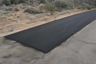 Fresh black asphalt repair patch next to arid soil and desert brush in Prescott, AZ.