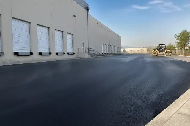 Freshly paved asphalt loading dock at a warehouse in Peoria, AZ with a steamroller parked to the side.