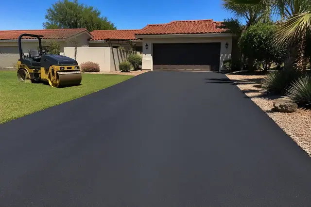 Newly paved asphalt driveway at a residential home in Tempe, AZ with a steamroller parked on the grass.