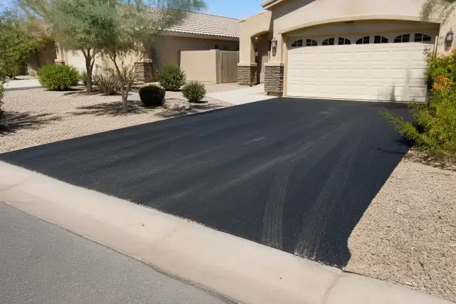 Freshly paved asphalt driveway meeting the street in a sunny Queen Creek, AZ neighborhood.