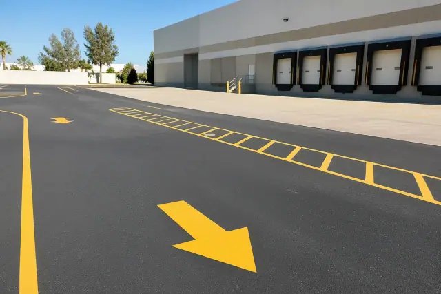 Freshly painted yellow directional arrows on the asphalt of a warehouse loading zone in Scottsdale, AZ.