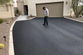 Contractor inspecting a freshly paved asphalt driveway by a stucco home in Scottsdale, AZ.