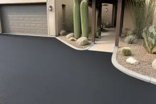 Freshly paved asphalt driveway meeting a concrete curb with saguaro cacti in Scottsdale, AZ.