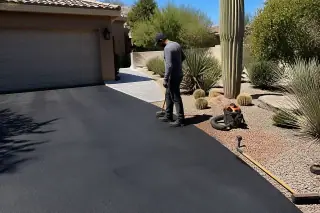 Worker inspecting a freshly sealcoated asphalt driveway by a garage and desert landscaping in Scottsdale, AZ.