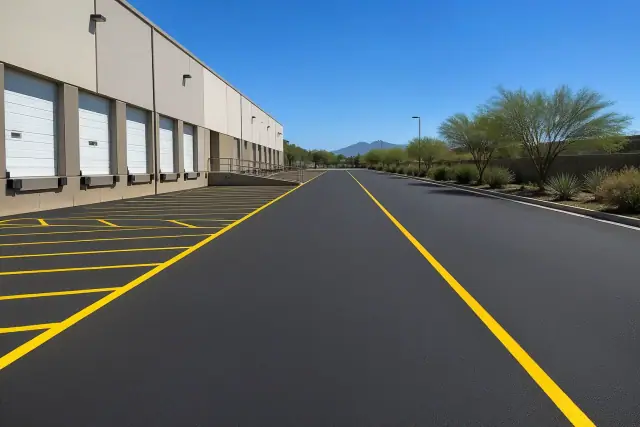Freshly paved asphalt loading zone with yellow parking lines at a warehouse in Scottsdale, AZ.