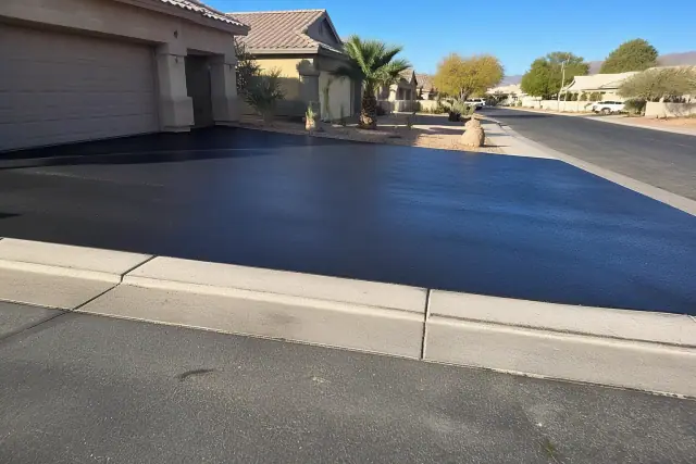 Freshly paved asphalt driveway meeting the concrete curb at a residential home in Peoria, AZ.