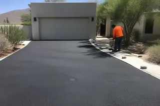 Technician cleaning a fresh asphalt driveway next to a residential garage in Scottsdale, AZ.
