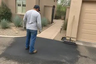 Technician inspecting a finished asphalt pothole repair at a house with desert landscaping in Scottsdale, AZ.