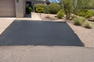 Finished asphalt pothole repair on a residential driveway near a garage and desert landscaping in Scottsdale, AZ.