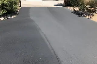 Fresh asphalt layer with a textured finish next to desert scrub on a residential street in Surprise, AZ.