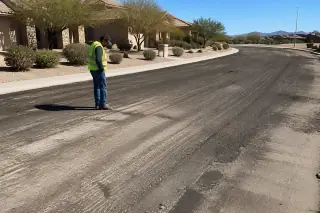 Contractor inspecting a textured asphalt sub-base after milling removal in Surprise, AZ.